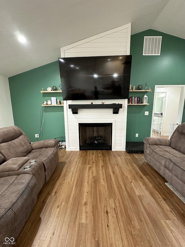 living area featuring visible vents, a large fireplace, lofted ceiling, and wood finished floors