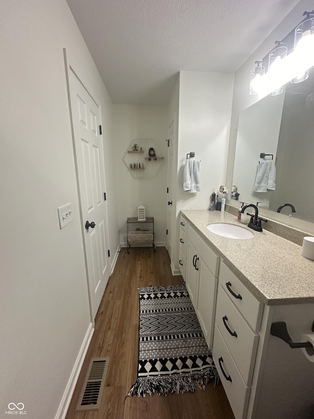 bathroom with visible vents, vanity, wood finished floors, baseboards, and a textured ceiling