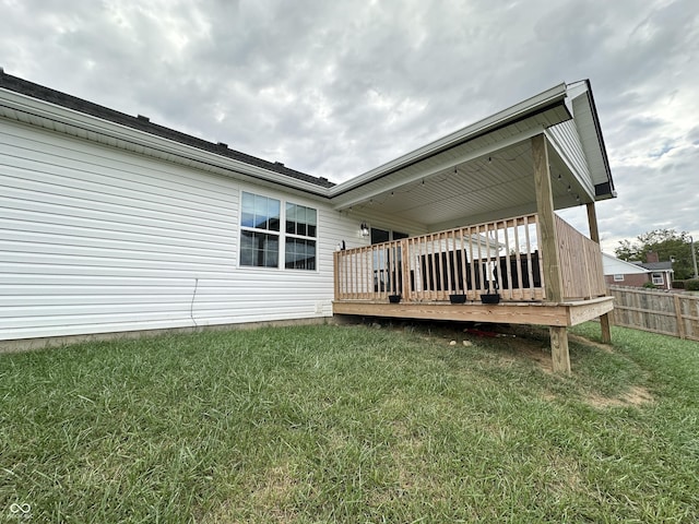 rear view of house with a lawn, a wooden deck, and fence