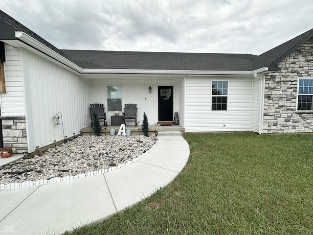 doorway to property with a lawn, covered porch, roof with shingles, and stone siding