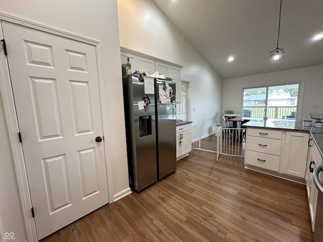 kitchen featuring dark wood-style flooring, hanging light fixtures, stainless steel fridge, dark stone countertops, and white cabinetry