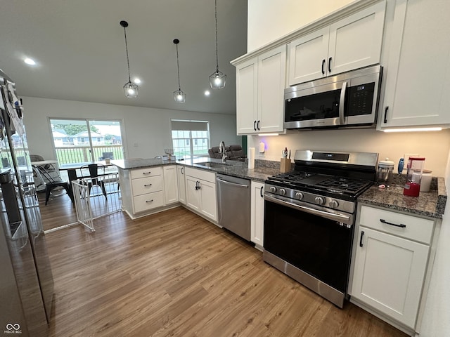 kitchen with a peninsula, appliances with stainless steel finishes, a sink, and light wood-type flooring