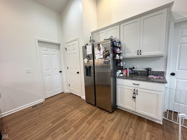 kitchen featuring stainless steel refrigerator with ice dispenser, a towering ceiling, visible vents, light wood-type flooring, and dark stone countertops