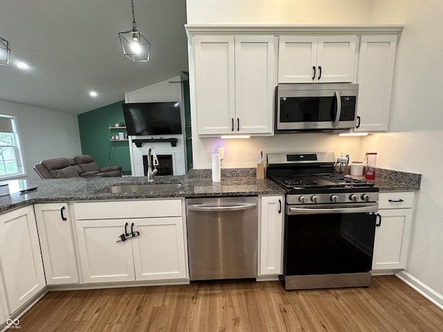 kitchen featuring open floor plan, a sink, light wood-style flooring, vaulted ceiling, and stainless steel appliances