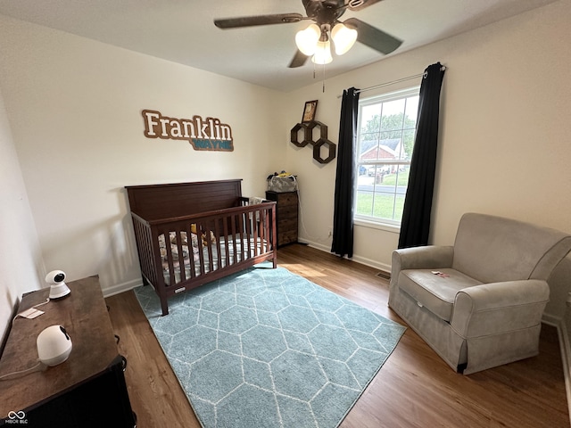 bedroom featuring ceiling fan, a nursery area, baseboards, and wood finished floors