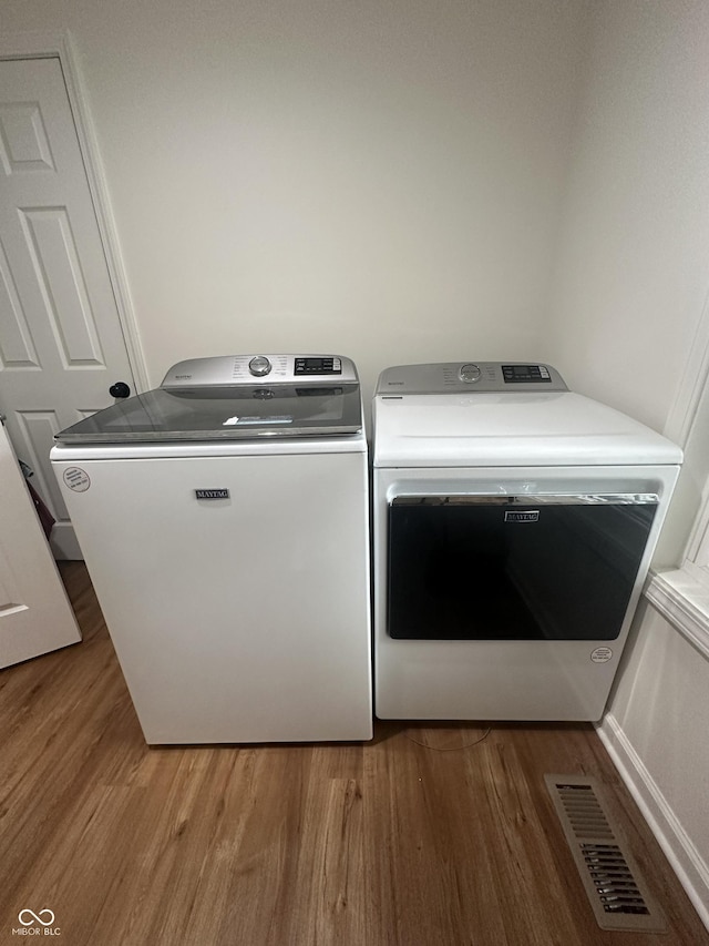 clothes washing area with laundry area, independent washer and dryer, wood finished floors, and visible vents
