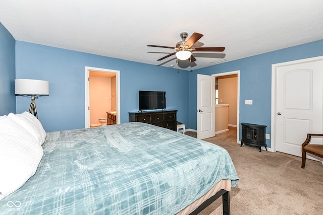 bedroom featuring ceiling fan, ensuite bath, a wood stove, and light colored carpet