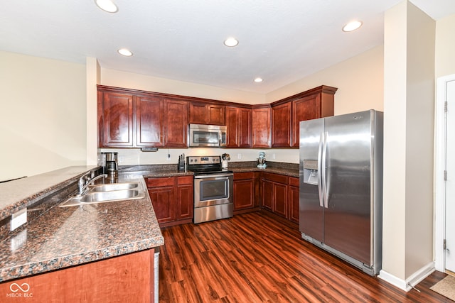 kitchen with appliances with stainless steel finishes, sink, kitchen peninsula, dark stone countertops, and dark hardwood / wood-style floors