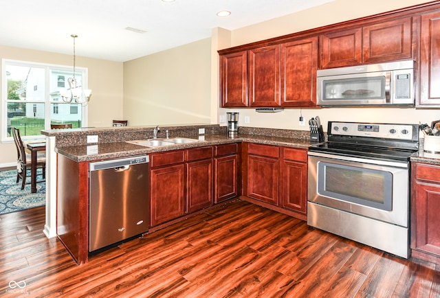 kitchen with appliances with stainless steel finishes, sink, kitchen peninsula, dark wood-type flooring, and a notable chandelier