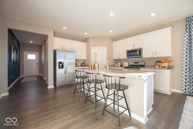 kitchen featuring dark wood-type flooring, a center island with sink, a kitchen bar, white cabinetry, and stainless steel appliances