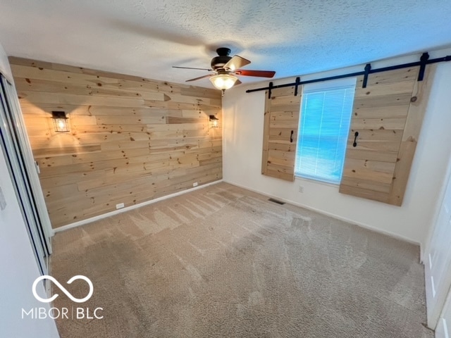 spare room featuring carpet, a barn door, ceiling fan, and wood walls