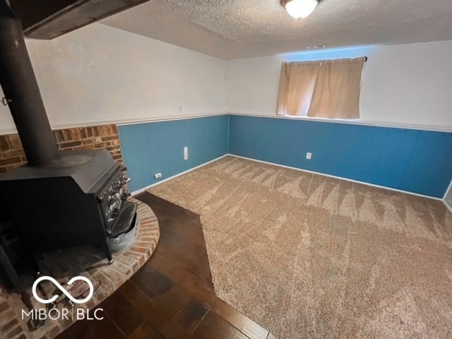 basement with a wood stove, a textured ceiling, and dark colored carpet