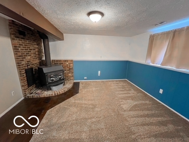 basement featuring a wood stove, a textured ceiling, and carpet floors