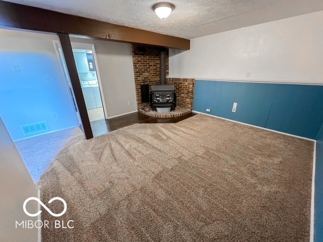 basement with a wood stove, a textured ceiling, and dark colored carpet