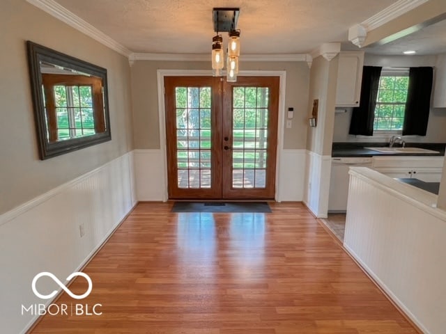 doorway to outside with a wealth of natural light, ornamental molding, french doors, and light hardwood / wood-style flooring