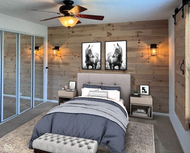 carpeted bedroom with a textured ceiling, a barn door, wooden walls, and ceiling fan