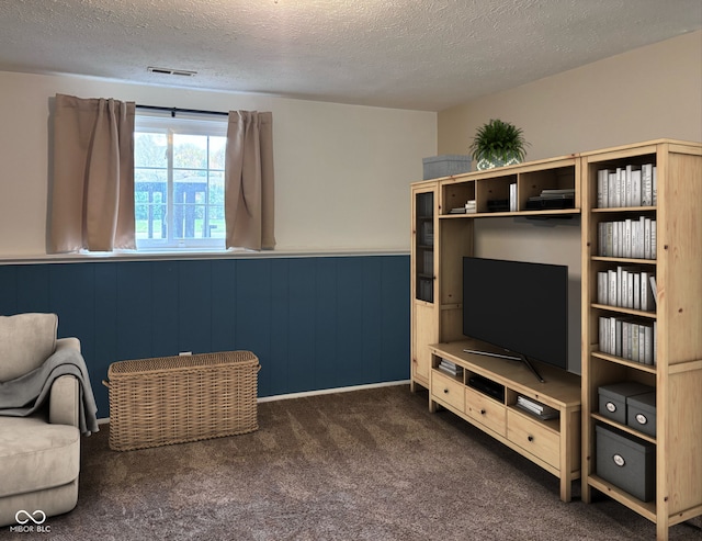 sitting room with dark colored carpet, a textured ceiling, and wood walls