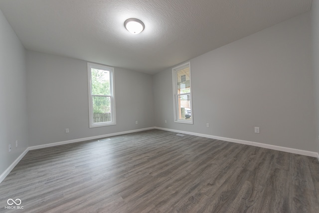 empty room featuring a textured ceiling, a healthy amount of sunlight, and dark hardwood / wood-style floors