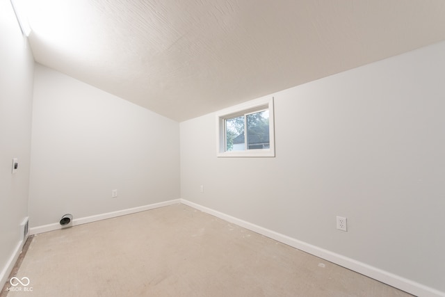 spare room featuring light carpet, vaulted ceiling, and a textured ceiling