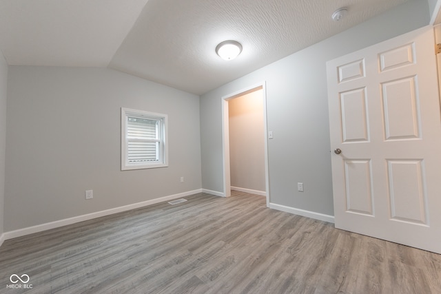 unfurnished bedroom with a textured ceiling, vaulted ceiling, and light hardwood / wood-style flooring