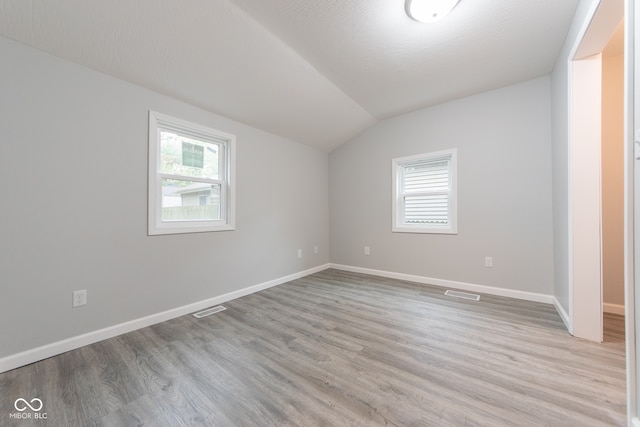 spare room featuring a textured ceiling, light hardwood / wood-style floors, and vaulted ceiling