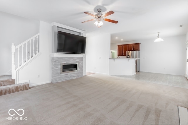 unfurnished living room featuring light carpet, a tiled fireplace, and ceiling fan