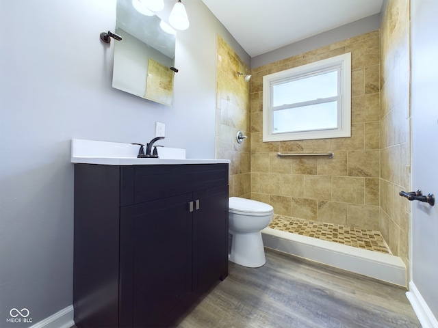 bathroom featuring a tile shower, vanity, hardwood / wood-style floors, and toilet