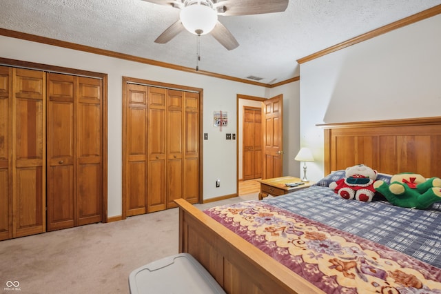 bedroom with a textured ceiling, light colored carpet, ceiling fan, multiple closets, and ornamental molding