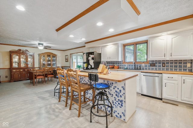 kitchen featuring plenty of natural light, wooden counters, stainless steel dishwasher, freestanding refrigerator, and crown molding