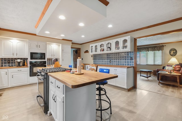 kitchen featuring butcher block counters, a breakfast bar area, ornamental molding, and black appliances