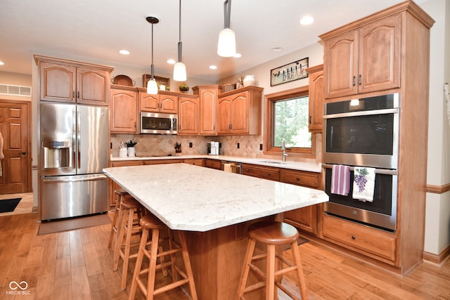 kitchen with sink, a kitchen island, appliances with stainless steel finishes, a kitchen breakfast bar, and light hardwood / wood-style floors