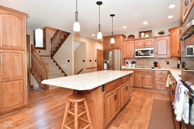 kitchen with light hardwood / wood-style floors, a kitchen island, backsplash, appliances with stainless steel finishes, and decorative light fixtures