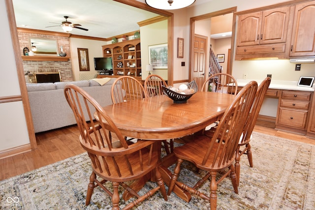 dining space with ceiling fan, light hardwood / wood-style flooring, a fireplace, and ornamental molding