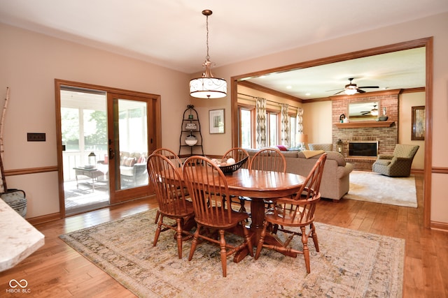 dining area with ornamental molding, a brick fireplace, light hardwood / wood-style floors, and ceiling fan