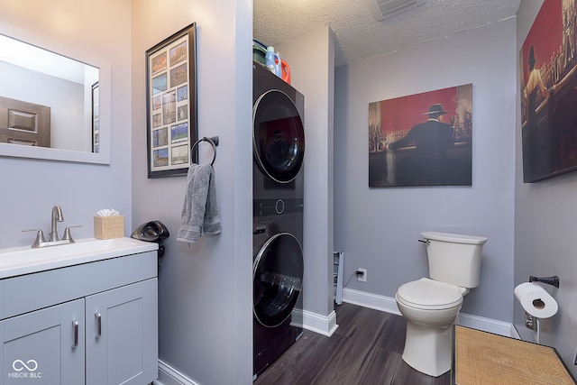 bathroom with vanity, wood-type flooring, stacked washer and clothes dryer, a textured ceiling, and toilet