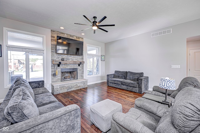 living room featuring dark hardwood / wood-style flooring, a stone fireplace, and ceiling fan