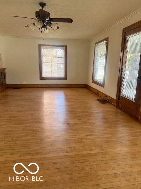 spare room with crown molding, light hardwood / wood-style floors, ceiling fan, and a wealth of natural light