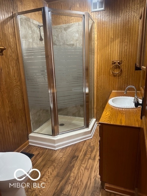 bathroom featuring wood walls, vanity, toilet, and a shower with door