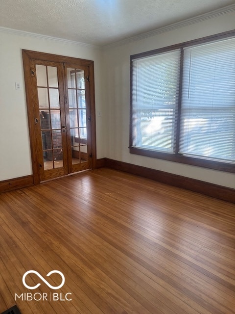 empty room featuring a textured ceiling, a healthy amount of sunlight, crown molding, and wood-type flooring