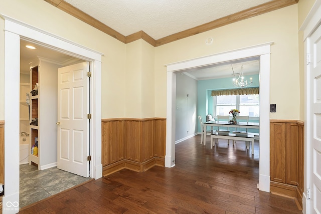 hallway with wood walls, ornamental molding, a textured ceiling, dark wood-type flooring, and a notable chandelier