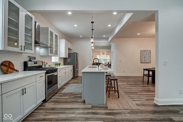 kitchen featuring sink, wall chimney exhaust hood, stainless steel appliances, a kitchen breakfast bar, and a center island with sink