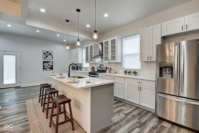 kitchen featuring an island with sink, wall chimney exhaust hood, stainless steel appliances, and white cabinets