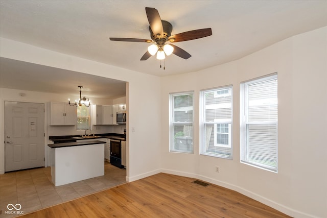 kitchen featuring white cabinetry, ceiling fan with notable chandelier, pendant lighting, light wood-type flooring, and a healthy amount of sunlight