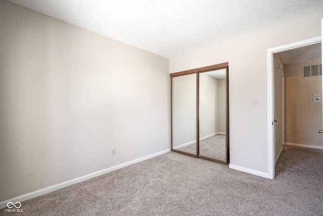 unfurnished bedroom with a closet, light colored carpet, and a textured ceiling