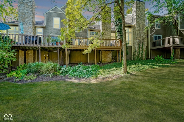 rear view of property with a chimney, a deck, and a lawn