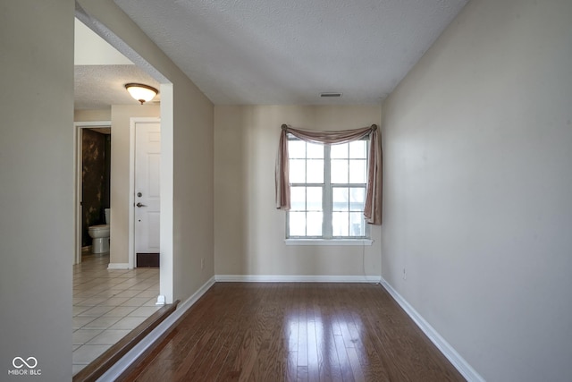 empty room with a textured ceiling, baseboards, visible vents, and light wood-style floors