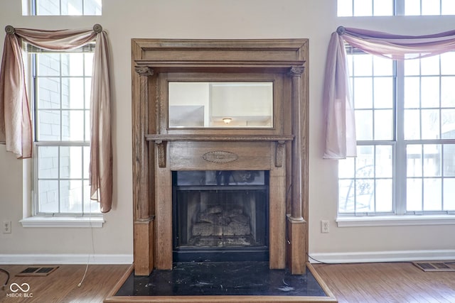 room details featuring a fireplace with flush hearth, wood finished floors, visible vents, and baseboards