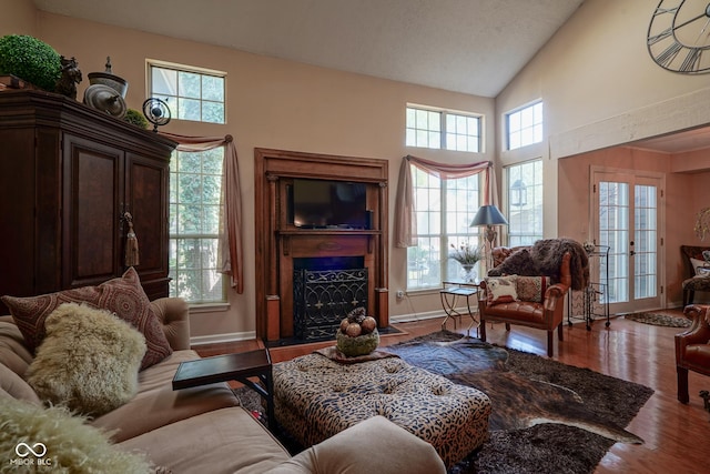 living room with a fireplace with flush hearth, high vaulted ceiling, baseboards, and wood finished floors