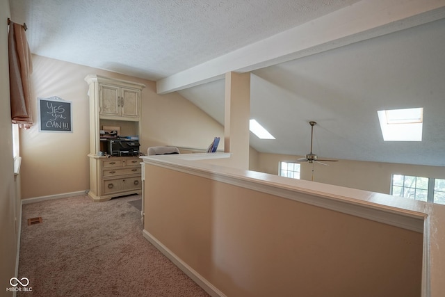 corridor featuring visible vents, light colored carpet, lofted ceiling with skylight, a textured ceiling, and baseboards