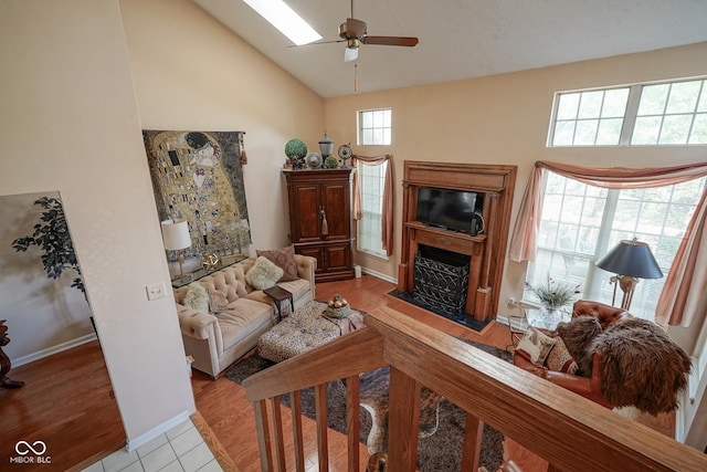 living room with high vaulted ceiling, a fireplace, a skylight, and light wood-style flooring